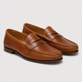 A pair of classic tan leather penny loafers with decorative stitching and braided trim across the vamp, displayed on a light gray background.