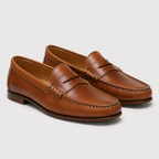 A pair of classic tan leather penny loafers with decorative stitching and braided trim across the vamp, displayed on a light gray background.