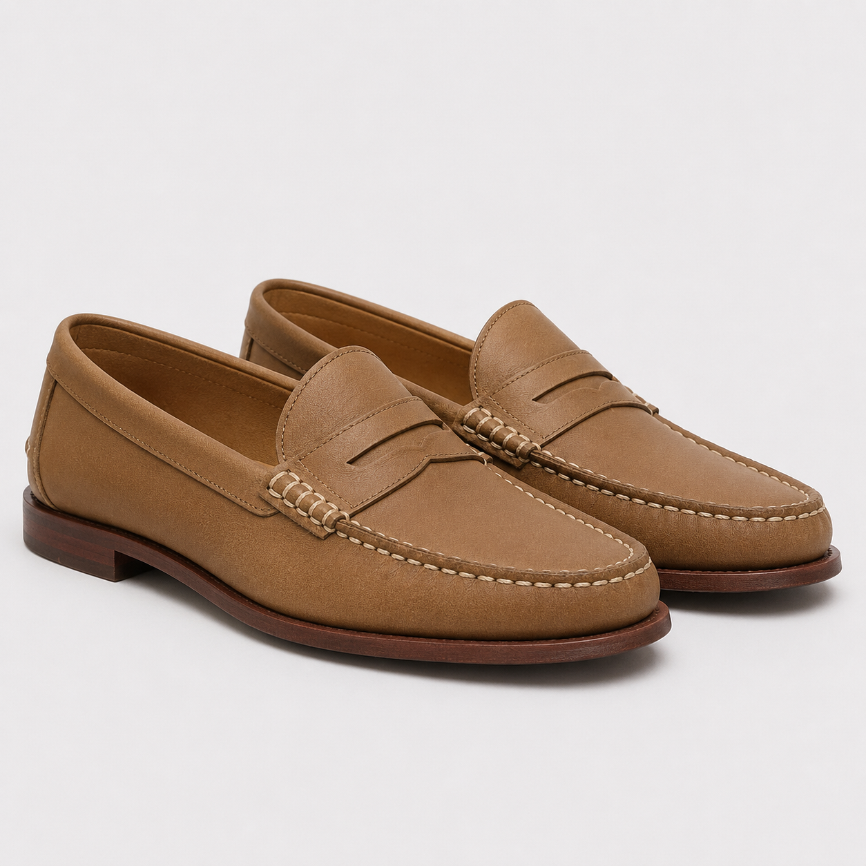 A pair of tan leather penny loafers with contrast stitching and a dark brown sole, photographed on a light gray background.