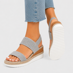 A pair of women's platform sandals with textured gray straps, a cork-wrapped midsole, and a white outsole, shown on a model's feet wearing light-wash jeans against a light gray background.