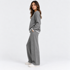 A woman modeling a gray knit lounge set with white contrast trim, featuring a crewneck sweater and matching wide-leg pants, photographed against a clean white studio background.