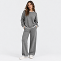 A woman modeling a matching gray knit lounge set with white trim, featuring a crewneck sweatshirt and wide-leg pants, against a plain white studio background.