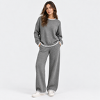 A woman modeling a matching gray knit lounge set with white trim, featuring a crewneck sweatshirt and wide-leg pants, against a plain white studio background.