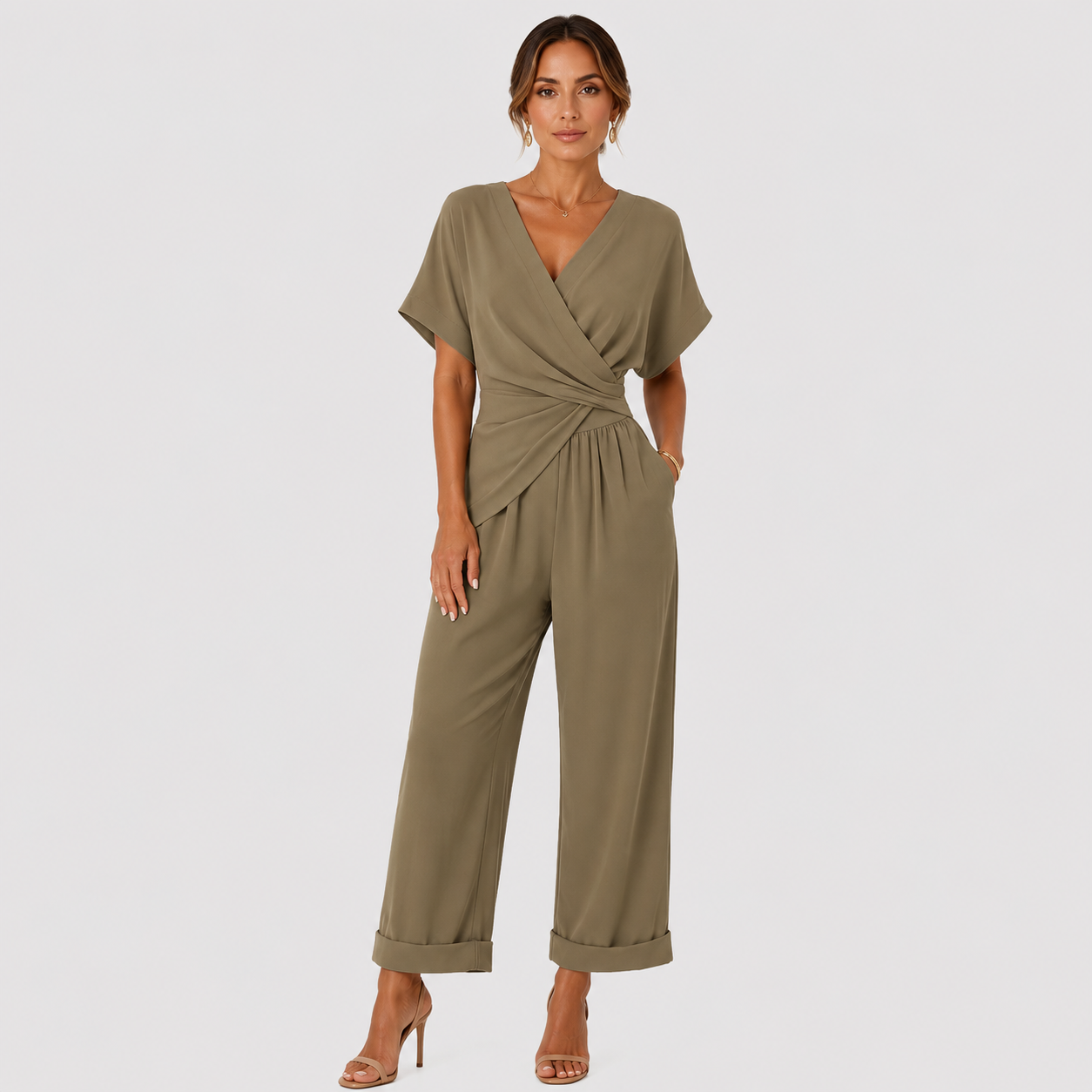 A woman modeling an olive green wrap-style jumpsuit with short sleeves and wide cropped legs, standing against a light gray studio background.