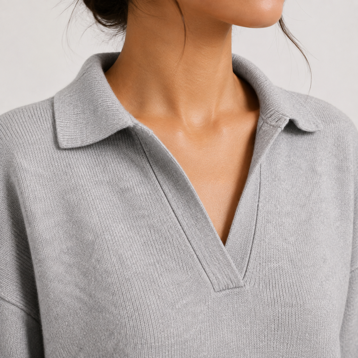 Close-up of a person wearing a light gray ribbed knit polo sweater with a collar and split V-neck.