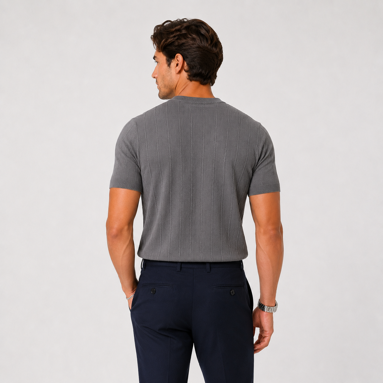 A man shown from the back wearing a gray ribbed short-sleeve t-shirt and navy blue trousers, standing against a light gray studio background.