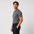 A man wearing a dark gray ribbed short-sleeve crewneck t-shirt and navy blue trousers, standing against a light gray studio background.