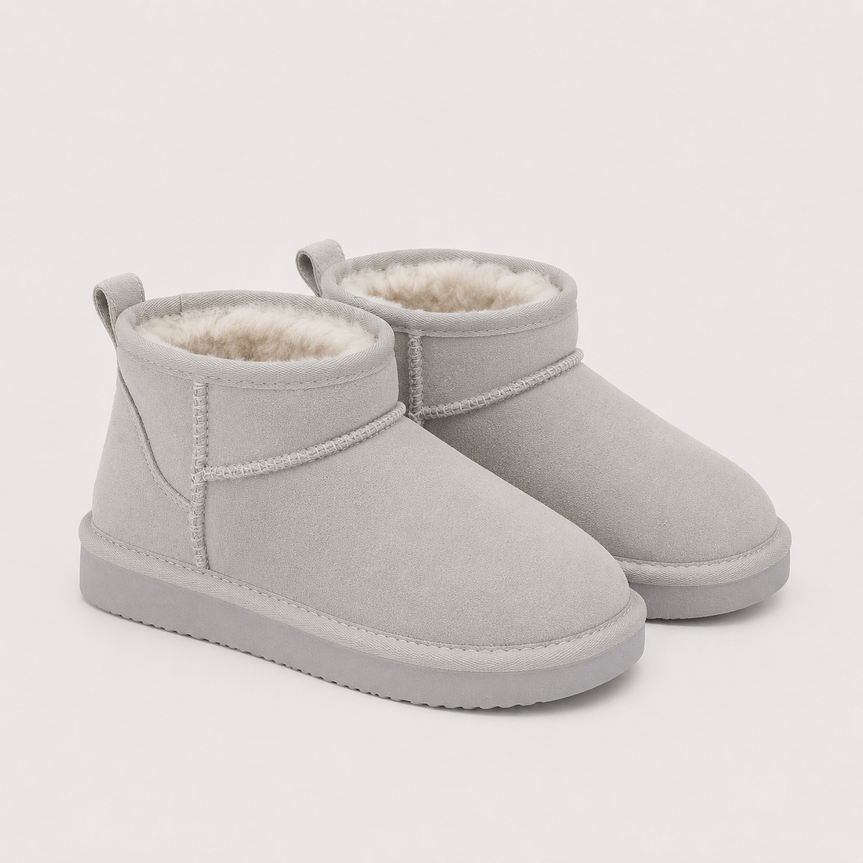 A pair of light gray suede ankle boots with a soft cream-colored shearling lining, shown on a clean off-white background.