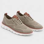 A pair of low-top lace-up sneakers in a muted taupe-beige color, featuring a textured knit upper, brown leather accents on the tongue and heel pull tabs, and a thick white sole with a dusty rose-pink stitched edge.