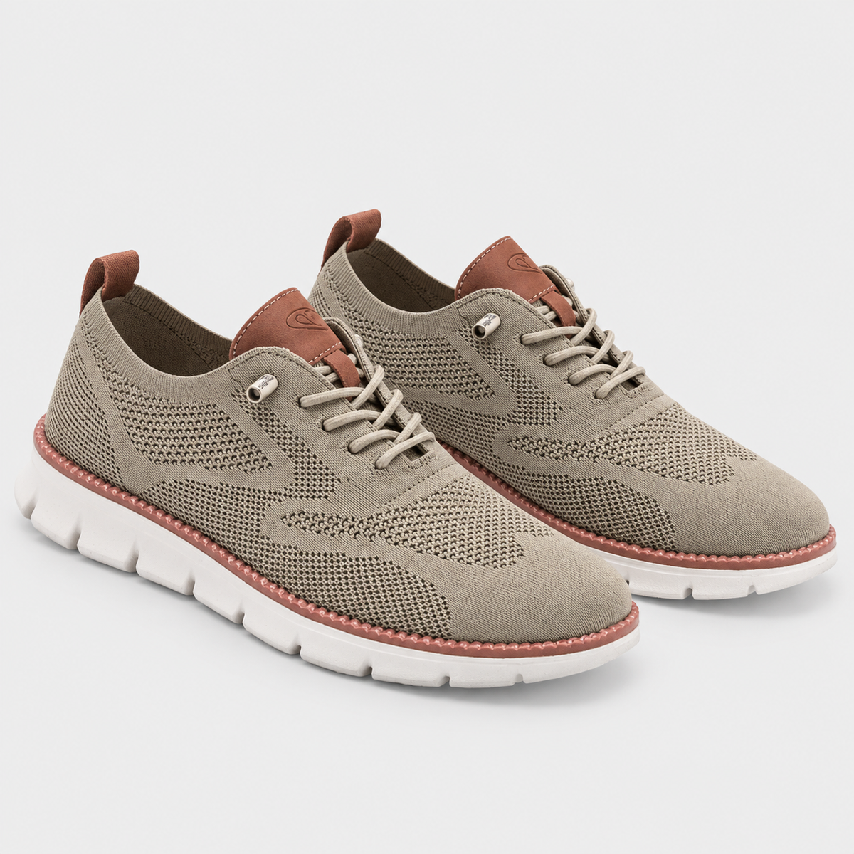 A pair of low-top lace-up sneakers in a muted taupe-beige color, featuring a textured knit upper, brown leather accents on the tongue and heel pull tabs, and a thick white sole with a dusty rose-pink stitched edge.