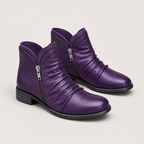 A pair of purple leather ankle boots with side zippers, shown on a light beige background.