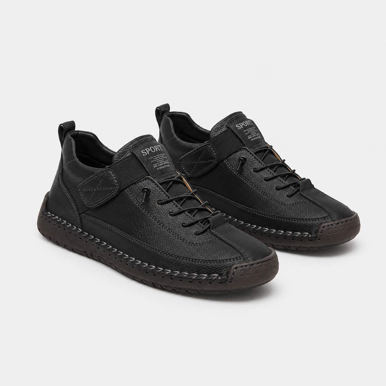 A pair of black low-top sneakers with a mix of leather and textured synthetic materials, featuring a hook-and-loop strap closure, laces, and a distinctive stitched midsole, shown on a light gray background.