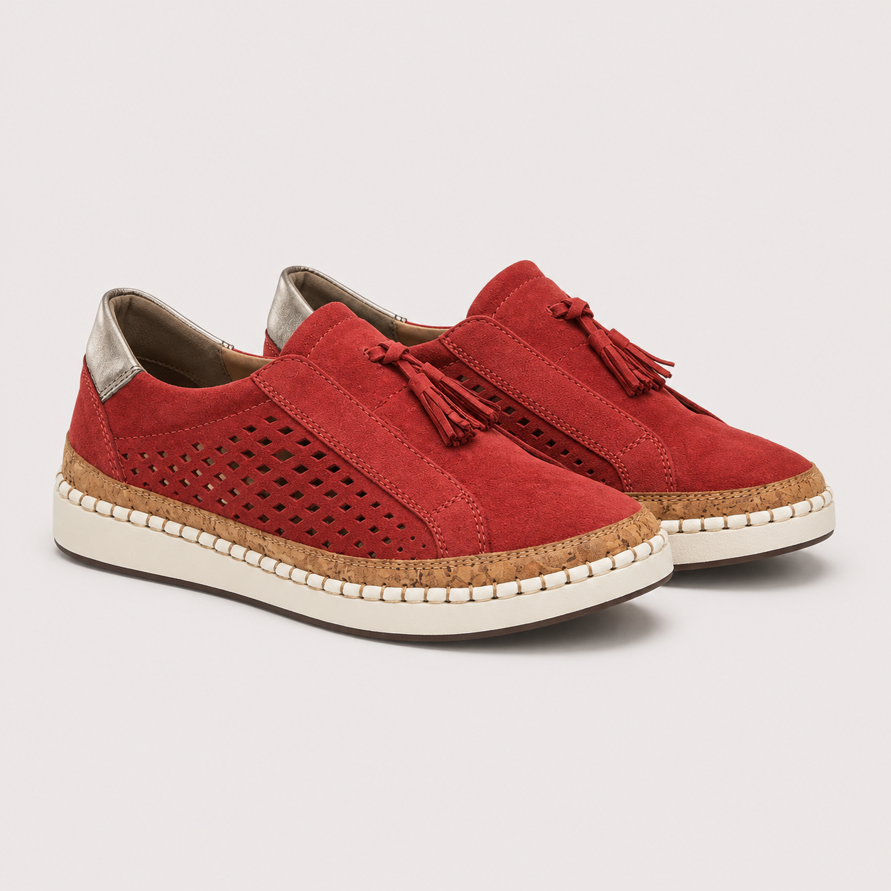A pair of red suede slip-on espadrille sneakers with perforated side panels, tassel details, cork-wrapped midsoles, and off-white soles, shown on a light gray background.