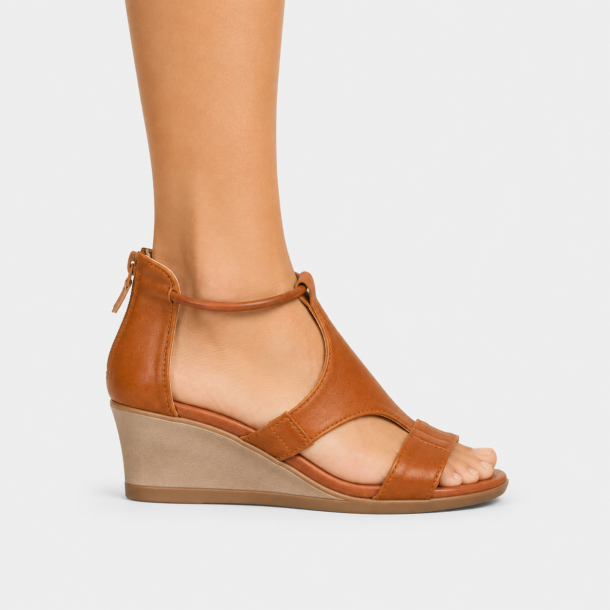 A woman's tan leather wedge sandal with an ankle strap and open toe, shown on a model's foot against a light gray background.