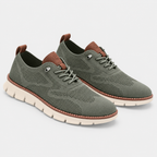 A pair of low-top knit sneakers in olive green with brown leather accents on the tongue, laces, and heel, featuring a cream-colored flexible sole, shown on a light gray background.