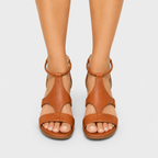 A pair of tan leather strappy sandals with low block heels, shown on a model's feet against a light gray background.