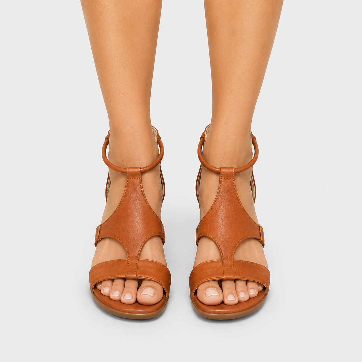 A pair of tan leather strappy sandals with low block heels, shown on a model's feet against a light gray background.