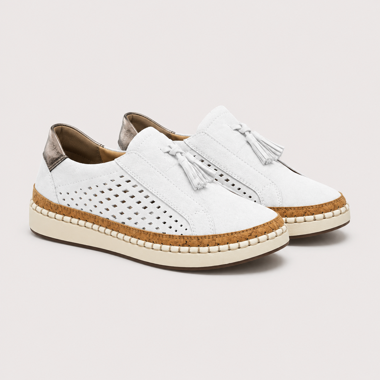 A pair of white slip-on espadrille-style shoes with perforated uppers, silver tassel details, cork midsoles, and cream-colored soles, shown against a light gray background.