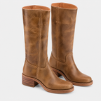 A pair of tall brown leather boots with a distressed finish, stacked block heels, and whipstitch detailing, shown against a light gray background.