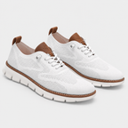 A pair of white mesh lace-up sneakers with brown leather accents on the tongue, heel pull tabs, and midsole stitching, shown against a light gray studio background.