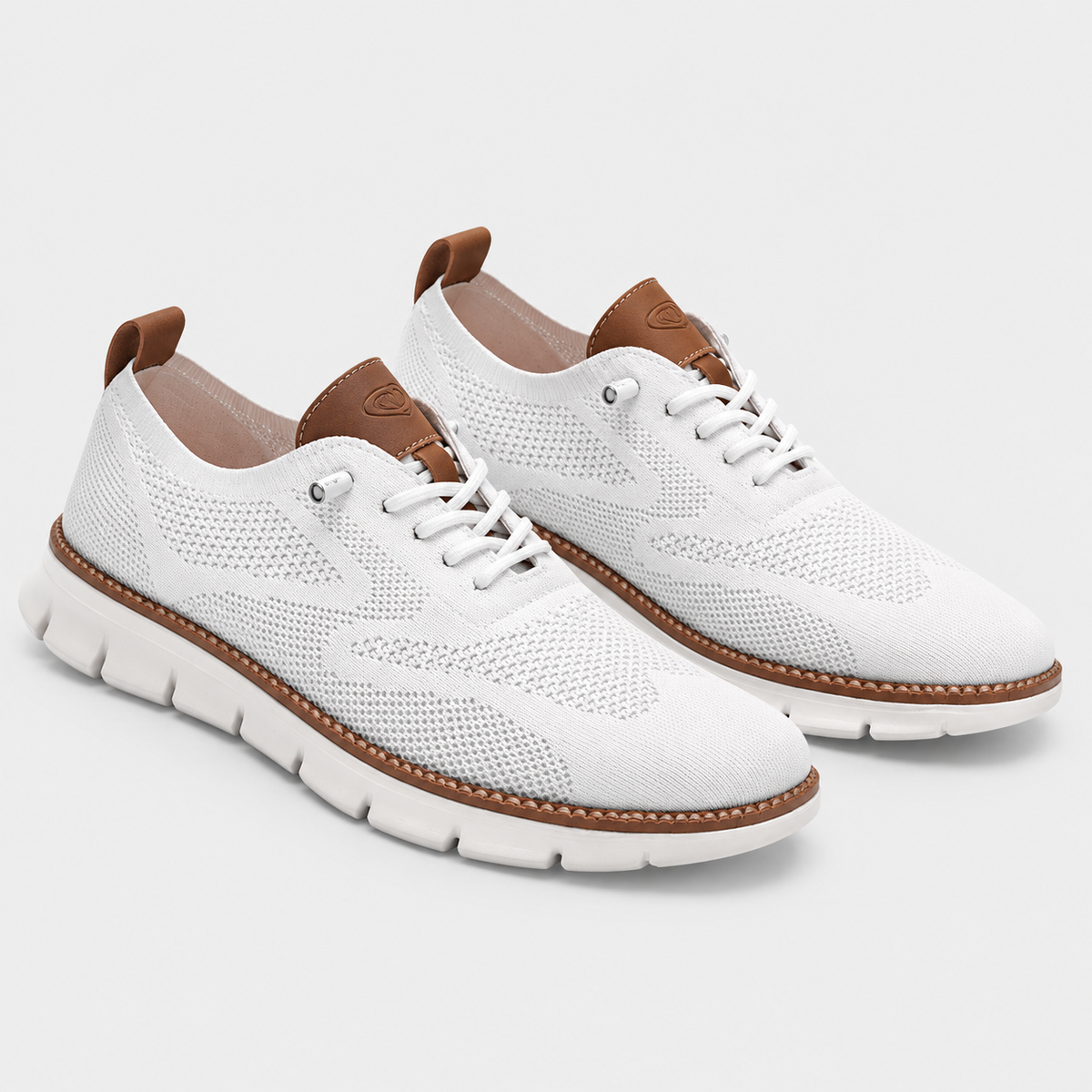 A pair of white mesh lace-up sneakers with brown leather accents on the tongue, heel pull tabs, and midsole stitching, shown against a light gray studio background.