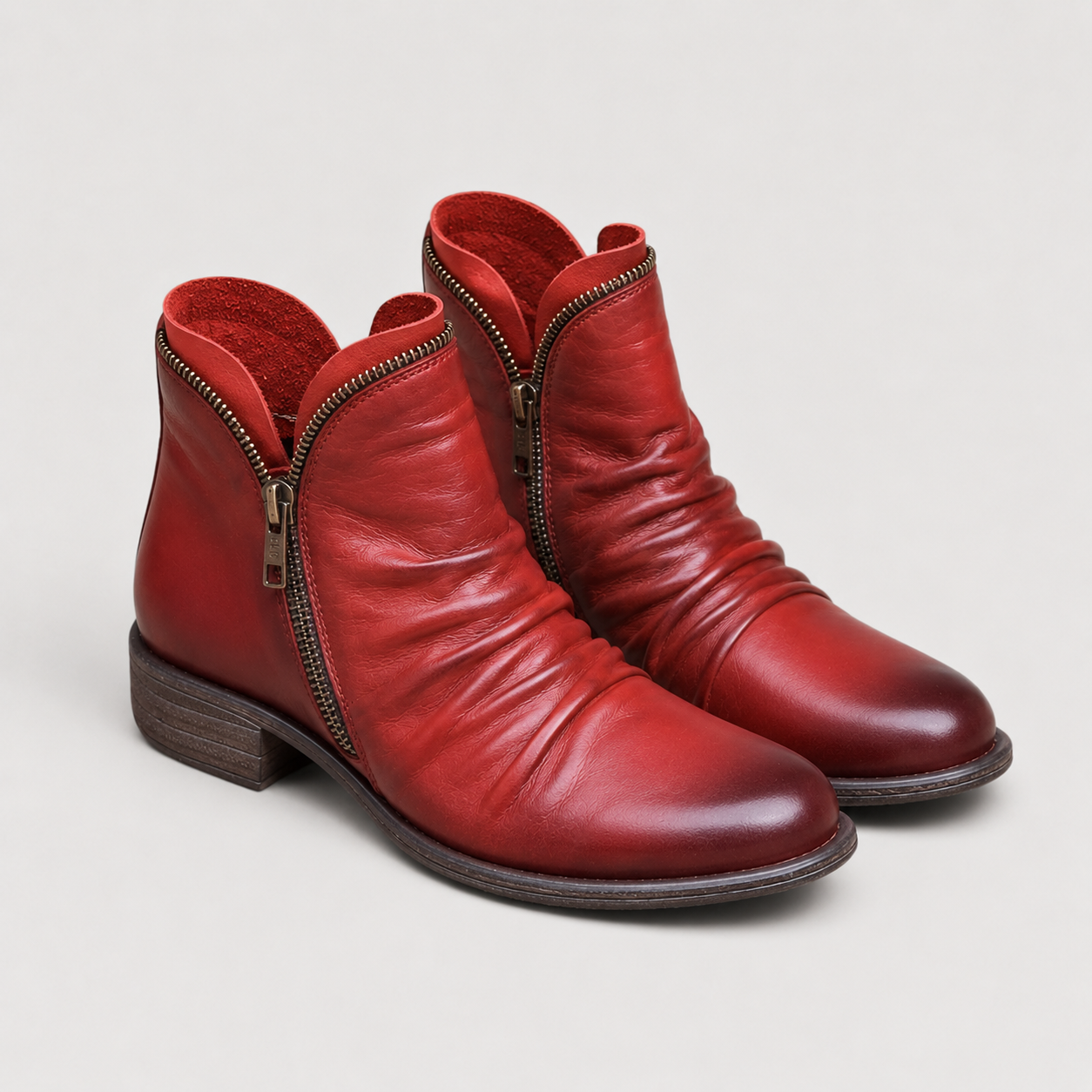 A pair of red leather ankle boots with a side zipper, dark brown stacked heels, and dark brown soles, photographed on a light gray background.