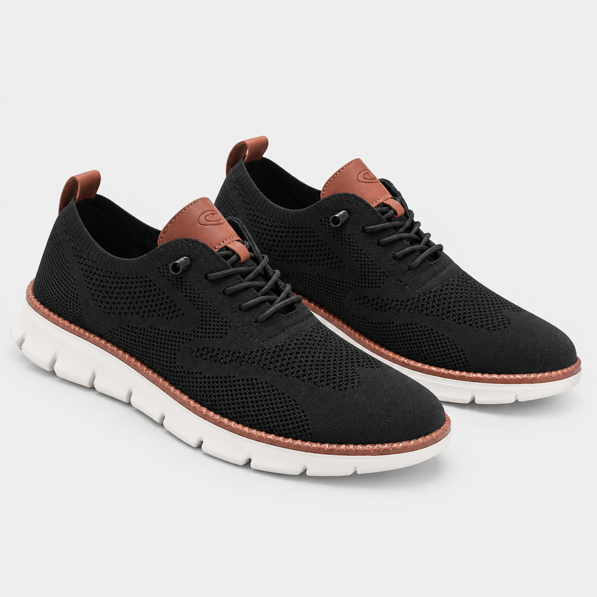 A pair of black mesh and suede low-top sneakers with brown leather accents on the collar, tongue, and heel pull tabs, and white soles, shown on a light gray background.