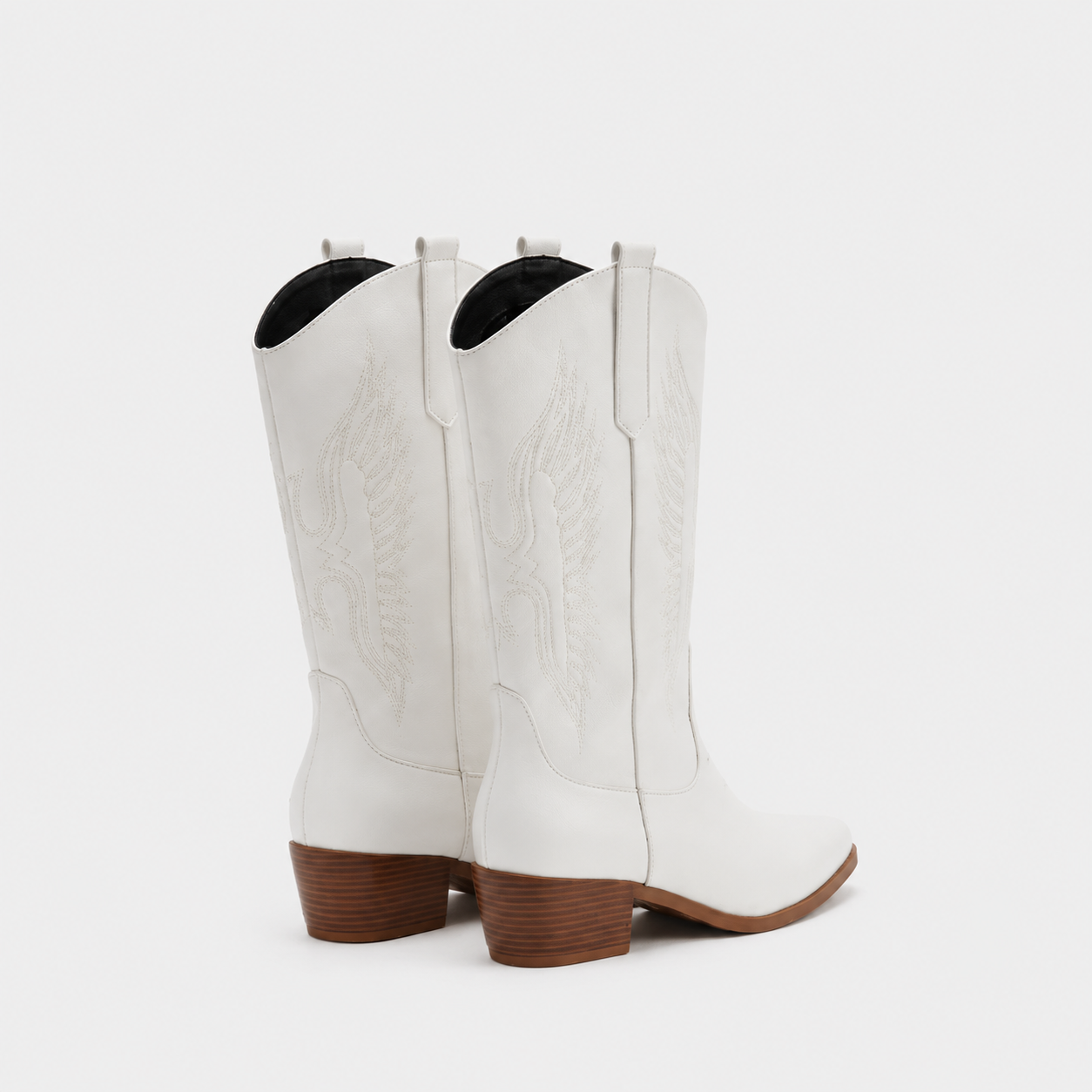 A pair of white leather cowboy boots with embossed western stitching and stacked brown block heels, shown from a rear three-quarter angle on a light gray background.