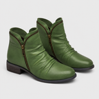 A pair of olive green leather ankle boots with a side zipper, dark brown stacked block heel, and gold-tone zipper pull, shown on a light gray background.