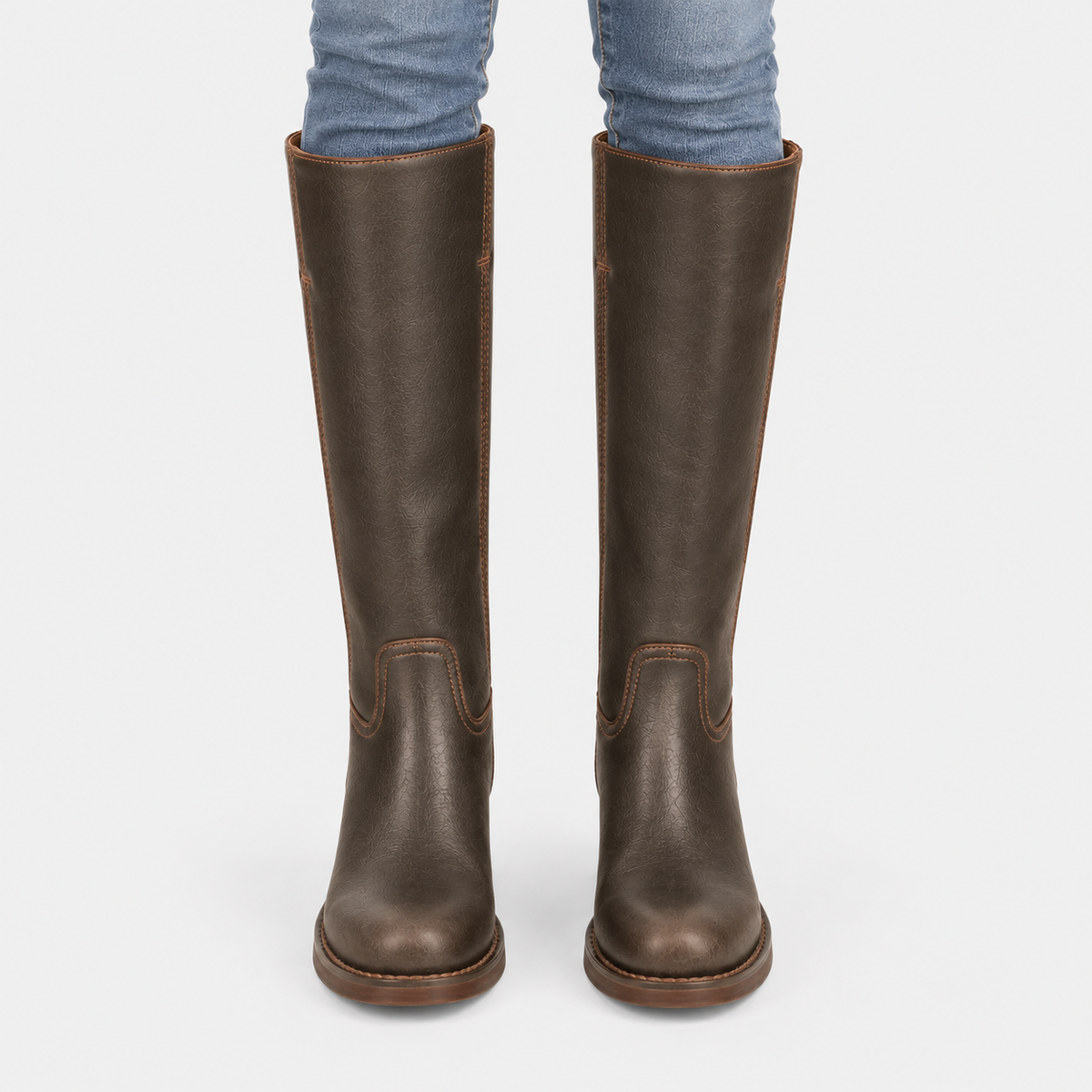 A pair of dark brown leather knee-high riding boots worn with blue jeans, shown from the back against a light gray background.