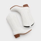 A pair of white leather western boots with tan stacked heels and toes, featuring white embroidered stitching on the shafts, shown on a light gray background.