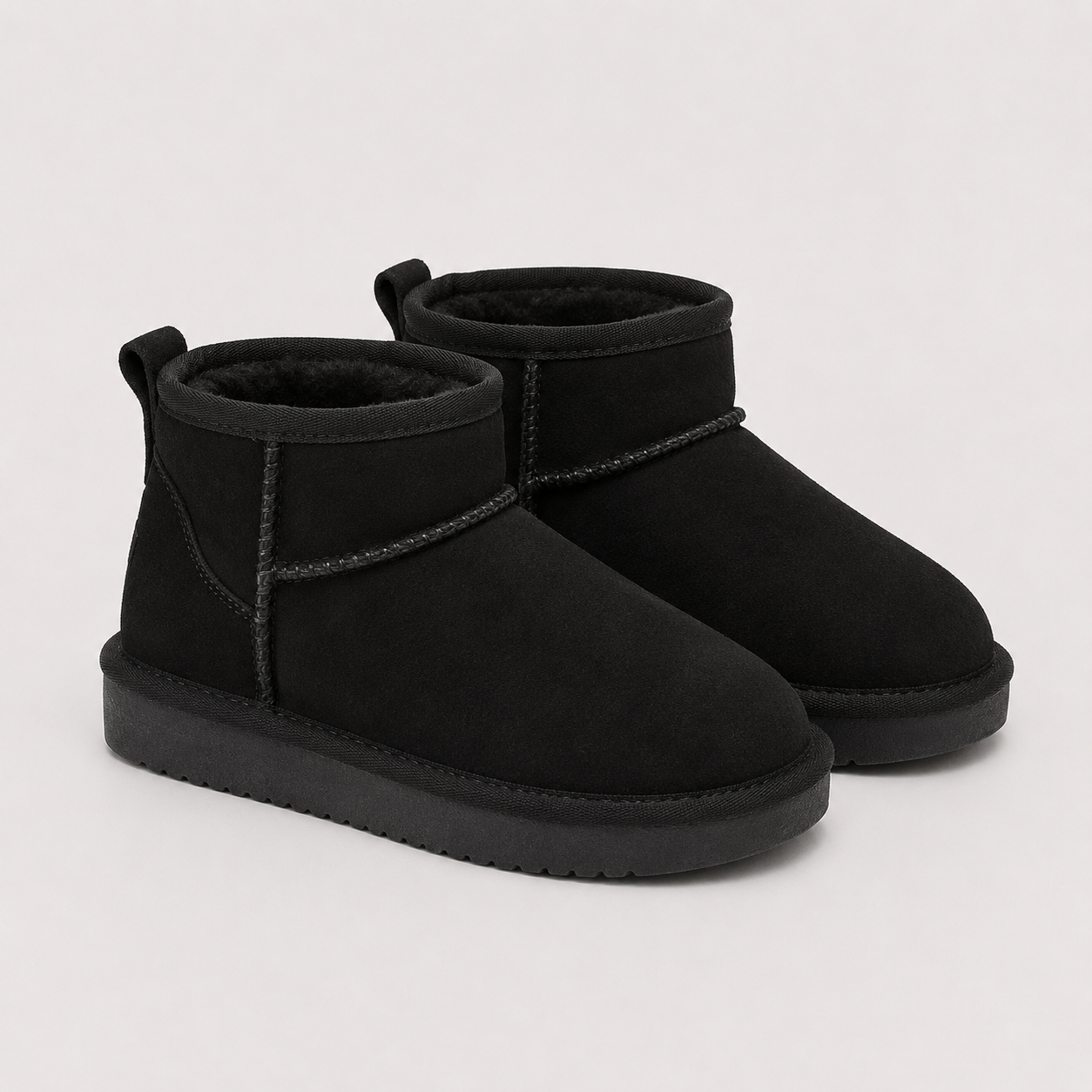 A pair of black suede ankle boots with black faux-fur lining and black soles, photographed on a clean, light gray background.