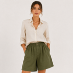 A woman modeling a light beige linen button-down shirt and olive green linen shorts against a plain off-white background.