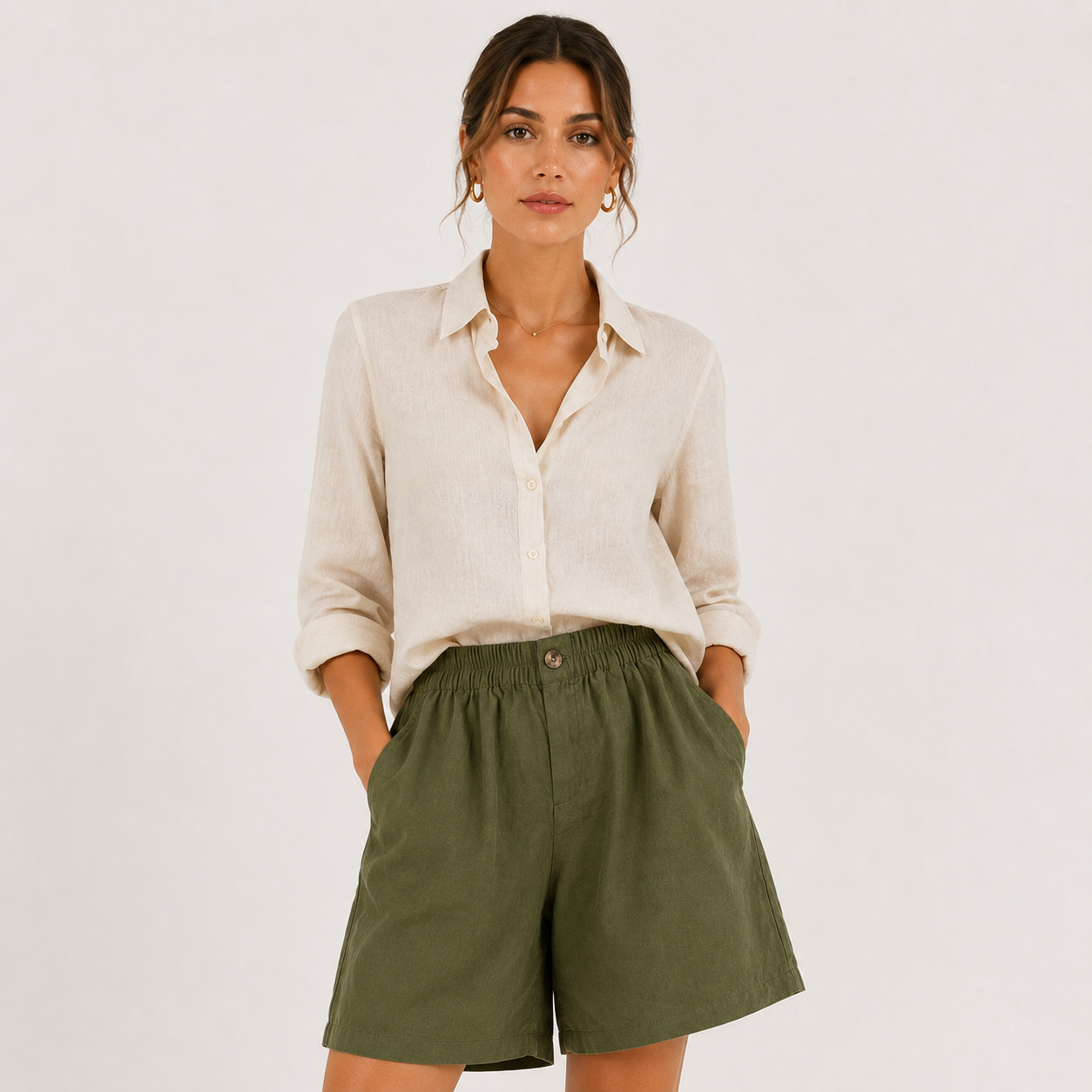 A woman modeling a light beige linen button-down shirt and olive green linen shorts against a plain off-white background.