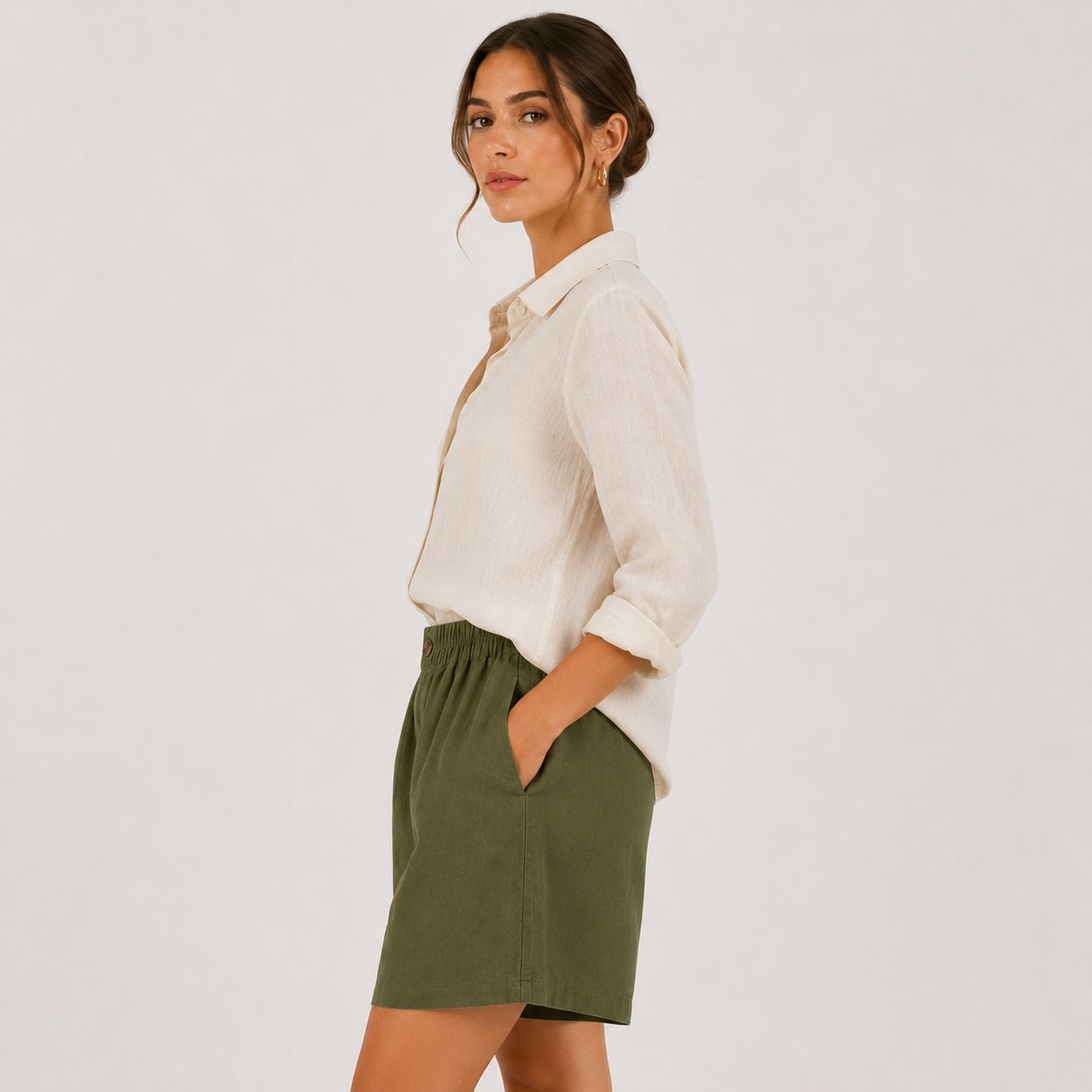 A woman wearing a white button-up shirt and an olive green skirt, photographed from the side against a plain light gray studio background.