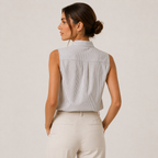 A woman shown from the back wearing a sleeveless, high-neck button-up shirt with fine vertical stripes in light gray and white, paired with cream-colored trousers, against a solid light beige studio background.