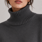 Close-up of a person wearing a dark charcoal gray ribbed turtleneck sweater, showing the collar texture and part of the face against a light neutral background.