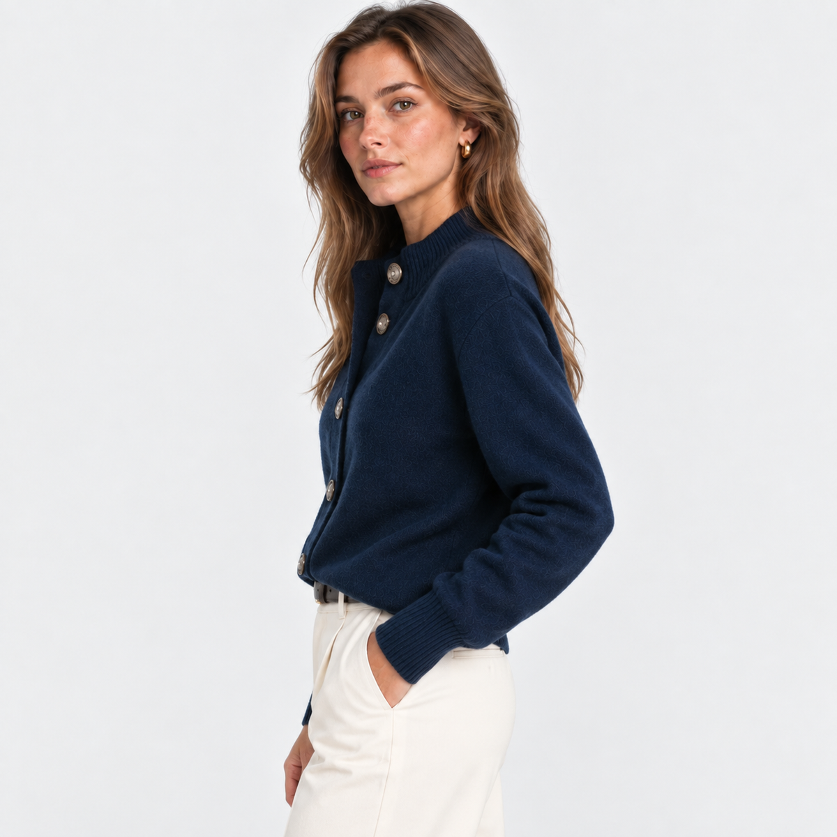 A woman wearing a navy blue knit cardigan with decorative buttons and cream trousers, photographed against a clean white studio background.
