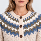 Close-up of a woman wearing a cream knit cardigan with blue and olive green Fair Isle style zigzag patterns and three brown buttons on the front.