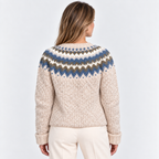 A woman viewed from the back wearing a cream-colored knit sweater with a blue, brown, and white Fair Isle yoke pattern, paired with cream pants, against a light gray studio background.