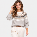A woman modeling a light gray knit sweater with a traditional Nordic-style pattern in cream, brown, and black, paired with cream trousers, against a solid light gray background.