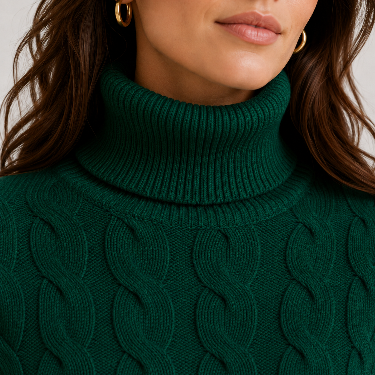 Close-up of a woman wearing a dark green ribbed turtleneck sweater with a cable-knit pattern, featuring gold hoop earrings.