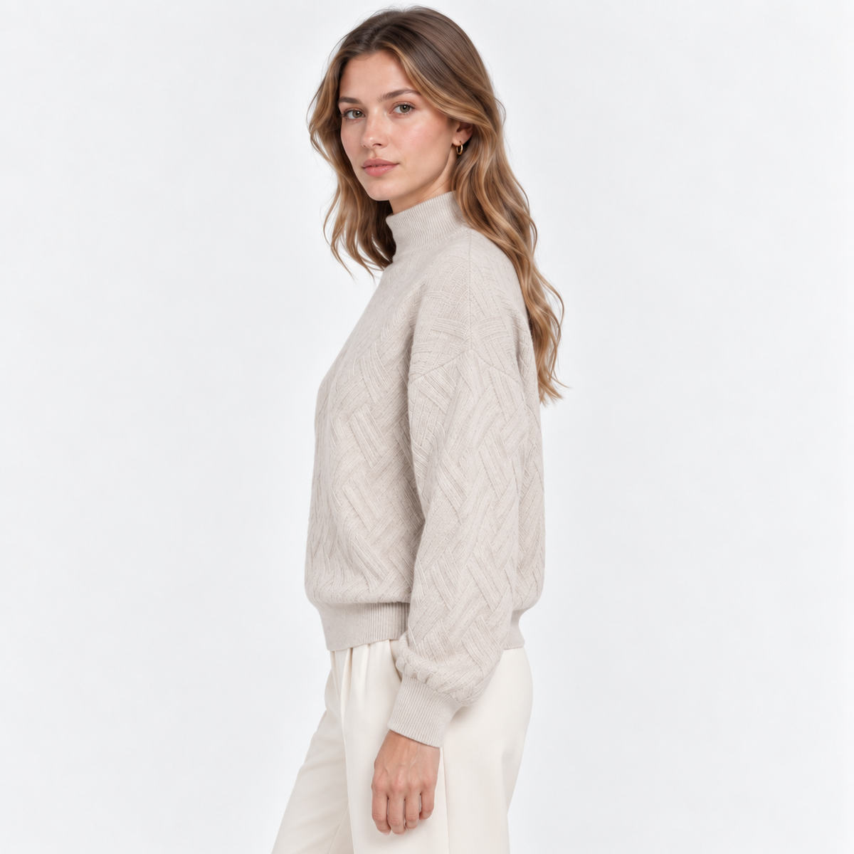A woman wearing a light beige cable-knit mock-neck sweater and cream trousers, shown from a side profile against a clean white studio background.