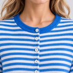 Close-up of a person wearing a blue and white horizontally striped knit cardigan with a ribbed crew neck and white buttons.