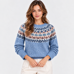A woman wearing a blue knit sweater with a multicolor Fair Isle pattern across the chest and cream pants, photographed against a clean white studio background.