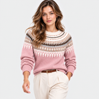 A woman modeling a pink Fair Isle knit sweater with cream, brown, and gray patterns across the chest and shoulders, paired with cream trousers, against a light gray studio background.
