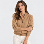 A woman wearing a camel-colored knit cardigan sweater with brown buttons, paired with white pants, photographed against a clean white studio background.