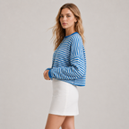 A woman modeling a blue and white striped long-sleeve knit top with a crew neck, paired with a white mini skirt, against a solid light gray studio background.