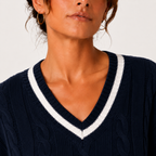 Close-up of a woman wearing a navy blue cable-knit V-neck sweater with a white contrast trim along the neckline.