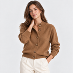 A woman modeling a camel brown button-up cardigan sweater with ribbed collar, cuffs, and hem, paired with off-white trousers, against a light gray studio background.
